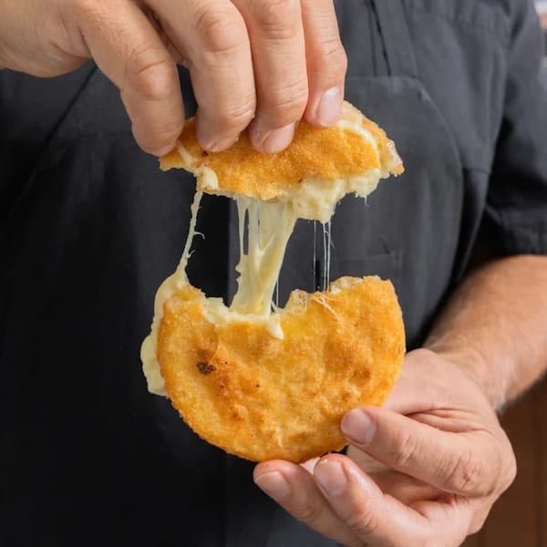 Hands pulling apart a golden-fried MASA empanada, revealing gooey, stretching white cheese inside.