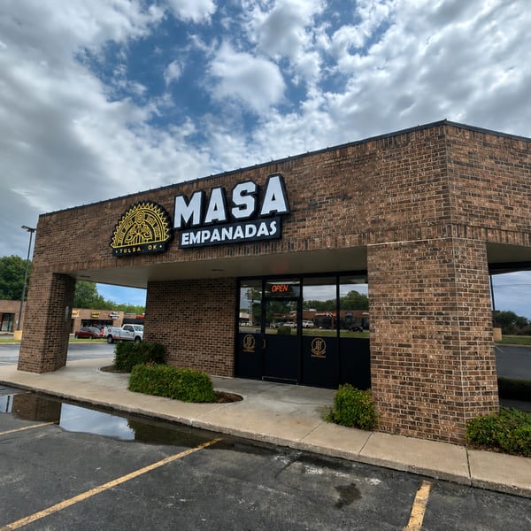Exterior of Masa Empanadas restaurant, a brick building with a large sign and glass entrance.