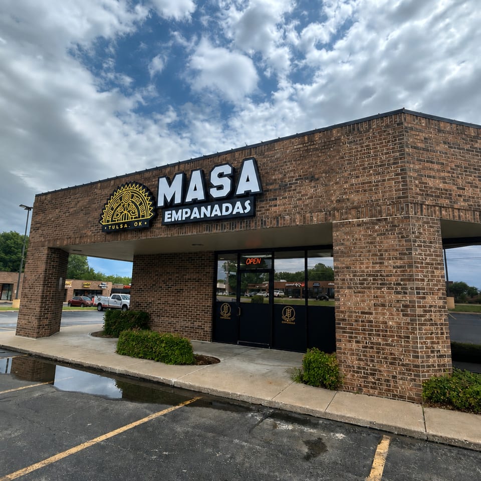 Exterior of Masa Empanadas restaurant, a brick building with a large sign and glass entrance.