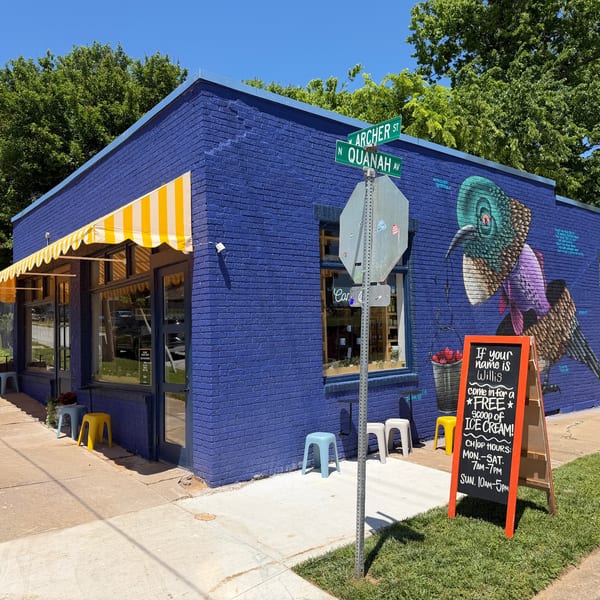 A vibrant blue building with a yellow striped awning, street signs, and a bird mural on its side.