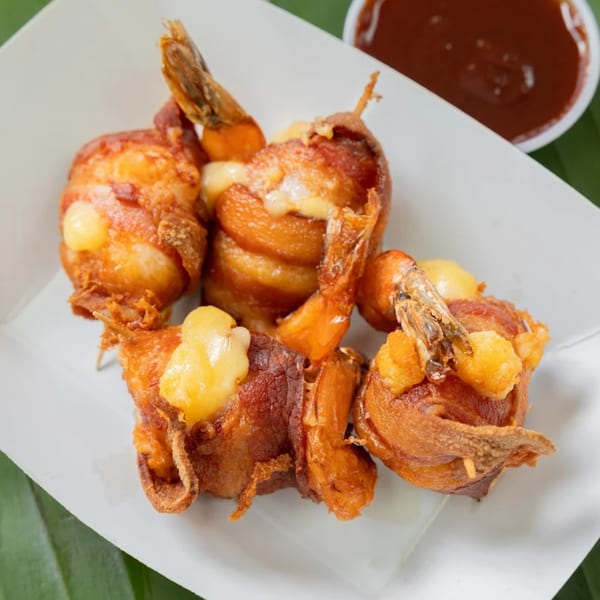 Bacon-wrapped shrimp with melted cheese and a side of dipping sauce in a white container.