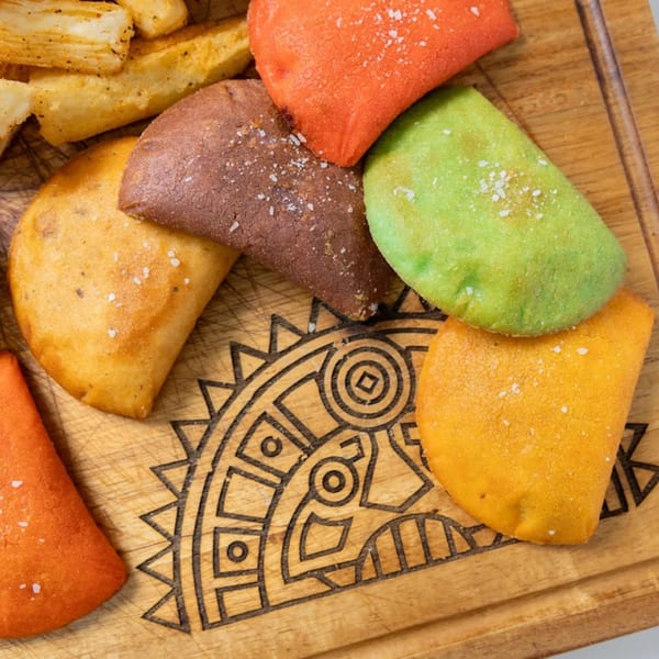 Colorful MASA Empanadas and yuca fries on a wooden board with an etched design.