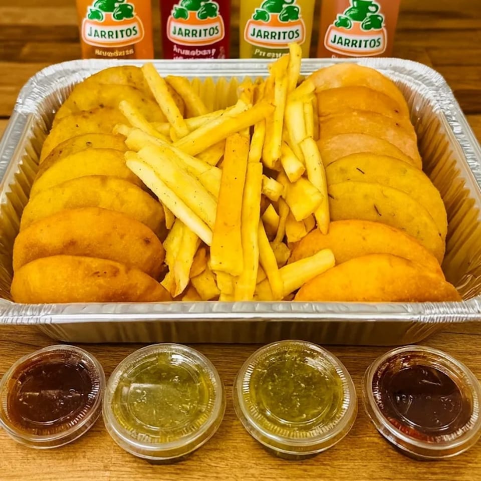 A foil tray of MASA Empanadas and fries, with four Jarritos sodas and dipping sauces.
